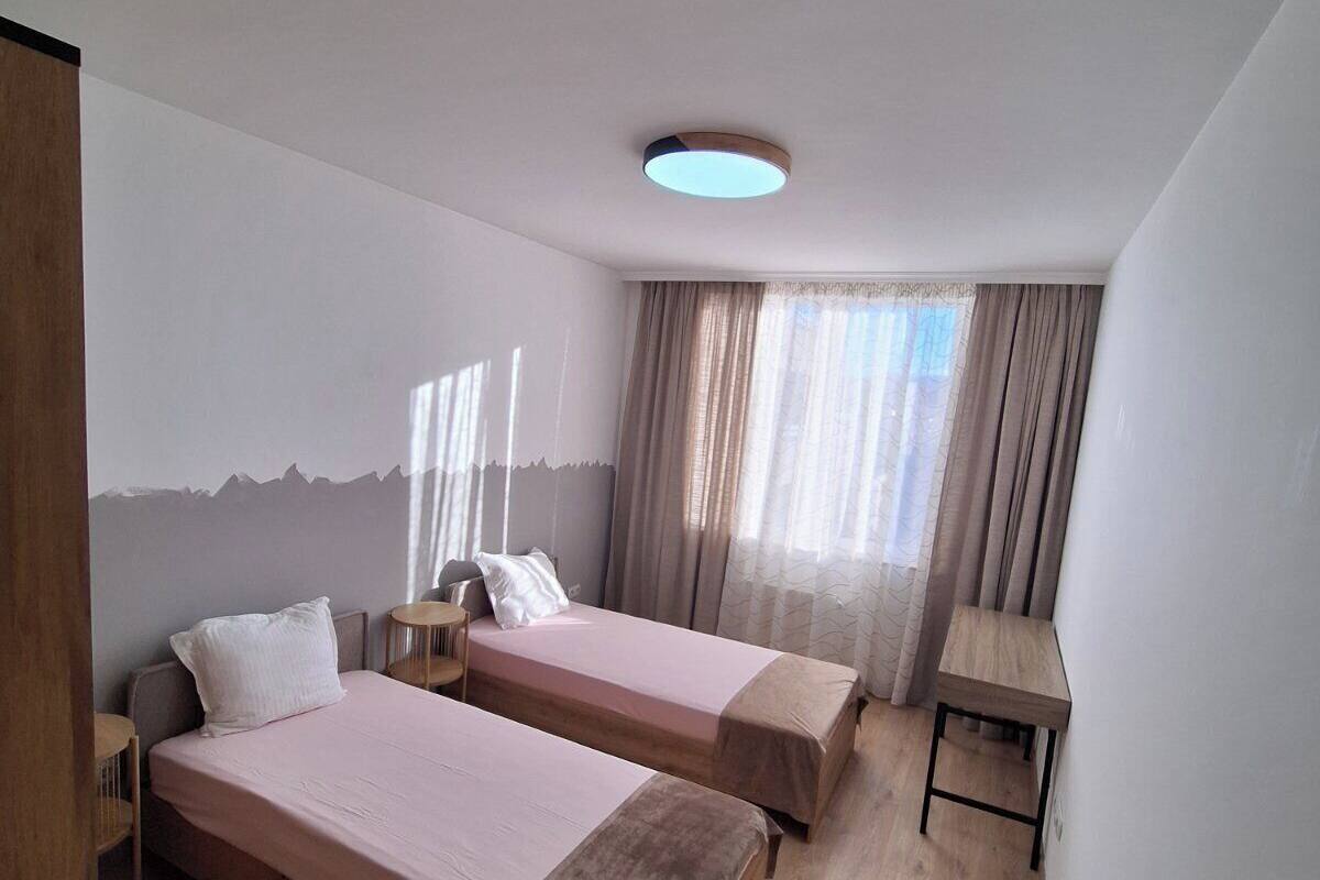 A hotel room with two beds, a desk, and a window with curtains.