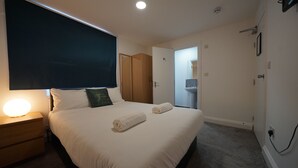 Un dormitorio con una cama grande, mesitas de noche, un televisor montado en la pared y una puerta que da al baño.