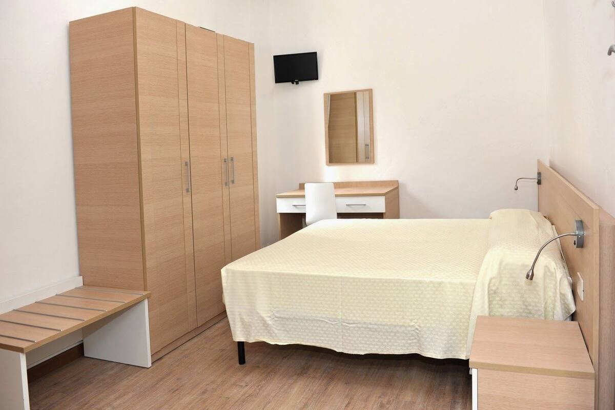 A bedroom with a bed, a desk, a wardrobe, and a TV.