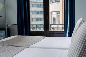 Una habitación de hotel con una cama, una ventana con cortinas y vistas a edificios.