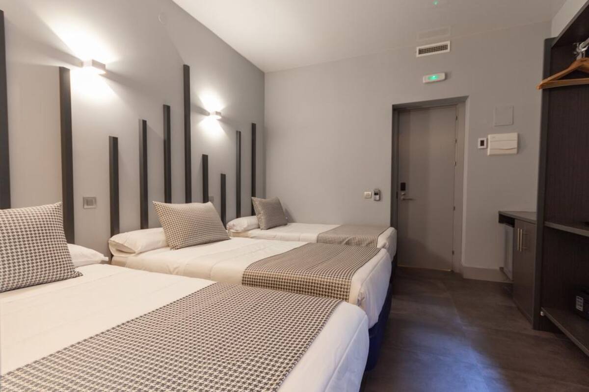 A hotel room with three beds arranged in a row, a wardrobe, and a door leading to another room.