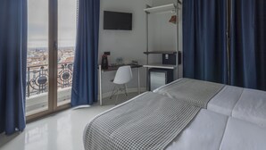 A hotel room with a bed, a desk, a chair, a TV, and a balcony with a view of the city. - Hostal El Carmen (Madrid)
