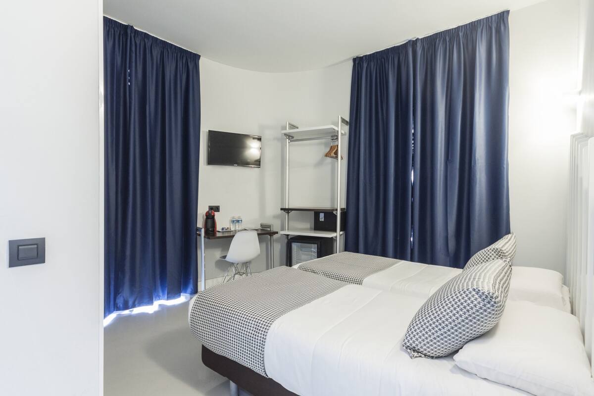 A hotel room with a bed, a desk, a chair, a mirror, and a television.