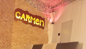 A modern sofa in a lobby with a brick wall and a neon sign that reads "CARMEN". - Hostal El Carmen (Madrid)