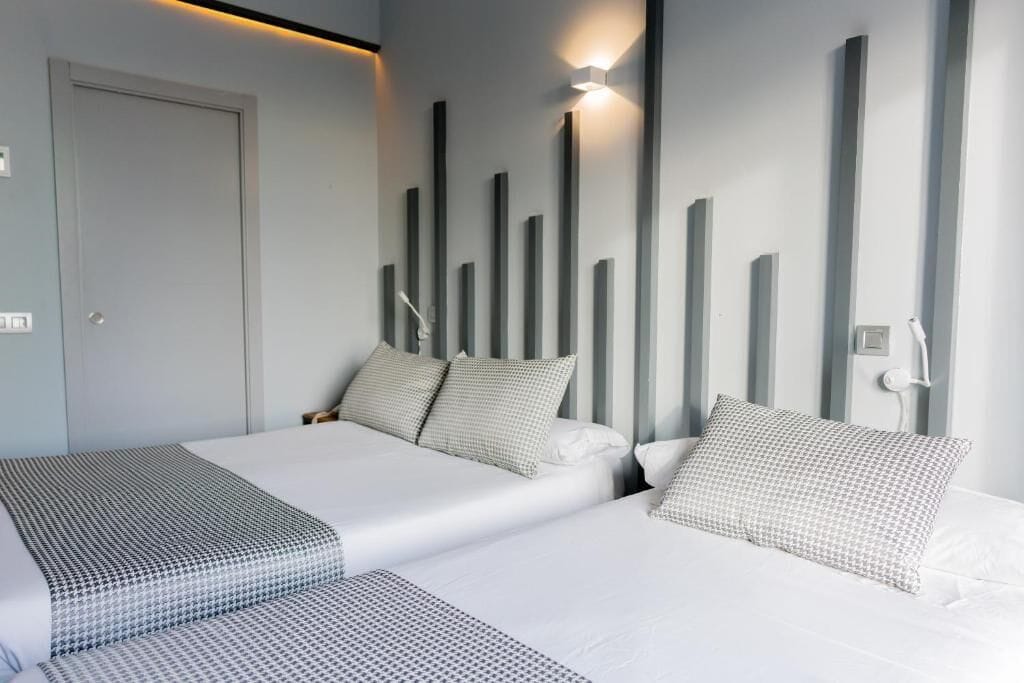 Una camera d'albergo moderna con un letto grande, un letto più piccolo e un comodino.