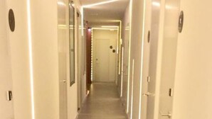 A long, narrow hallway with white walls and doors on both sides, leading to a door at the end. - Hostal El Carmen (Madrid)