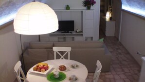 A dining area with a round table, white chairs, and a white sofa. There is a TV on a white cabinet in the background. - B&B La Grotta (Mesagne)