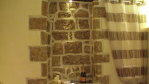 A bathroom with a stone wall, a bottle of champagne, and a candle on a shelf. - B&B La Grotta (Mesagne)