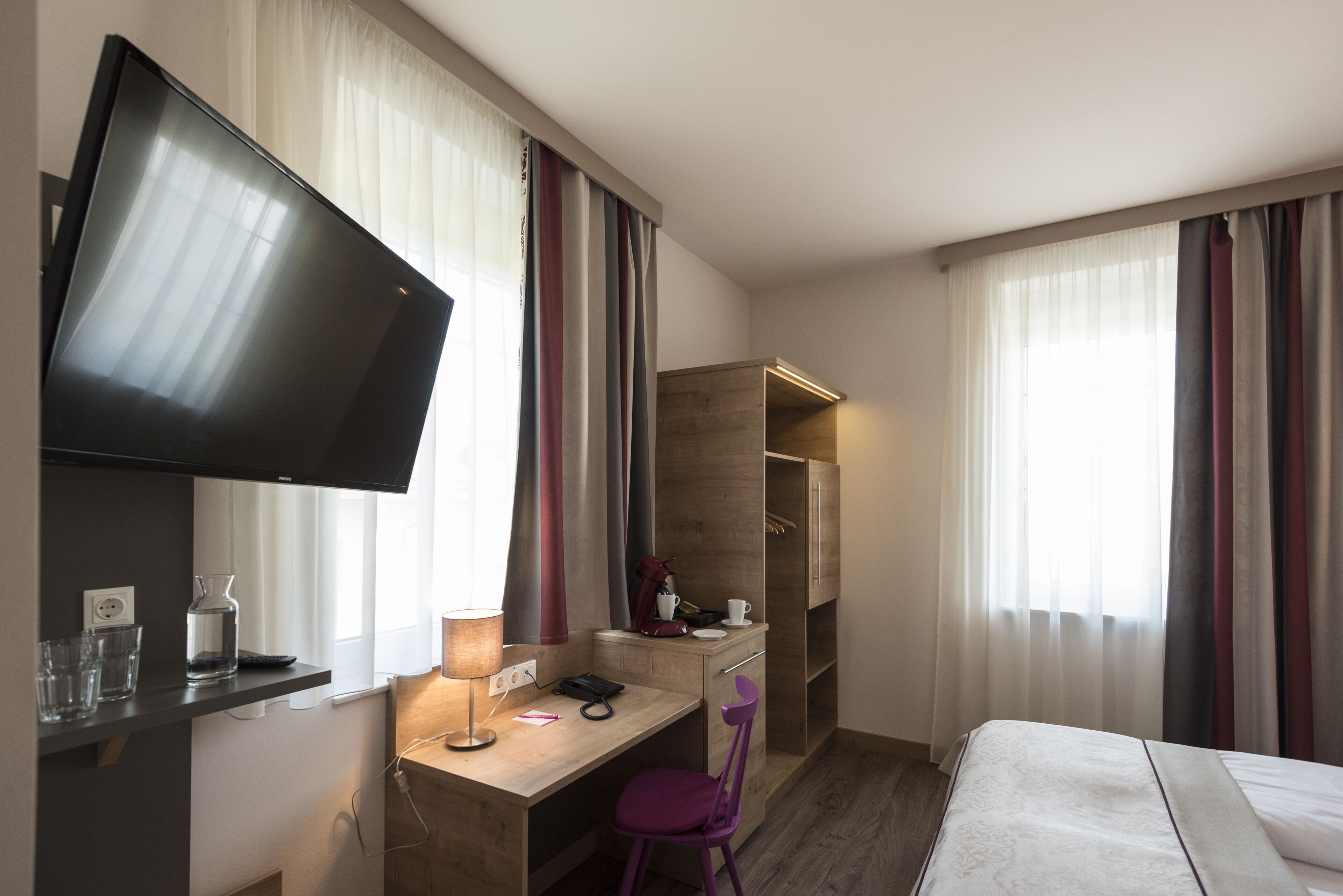 Ein Hotelzimmer mit einem Bett, einem Schreibtisch mit Stuhl, einem Fernseher und einem Kleiderschrank.