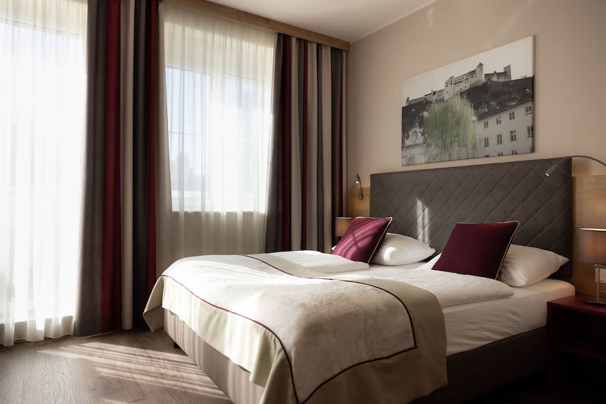A hotel room with a large bed, a headboard, a bedside table, and a window with curtains.