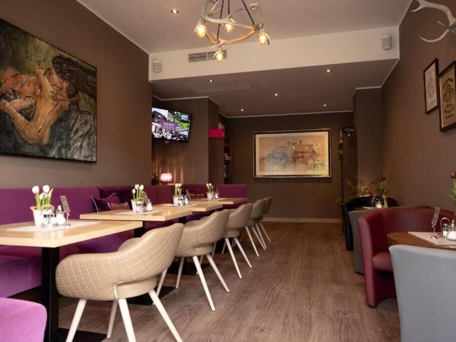 A restaurant with a long counter, cushioned seating, and a television screen.