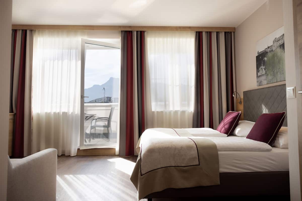 A hotel room with a bed, a chair, and a balcony with curtains.