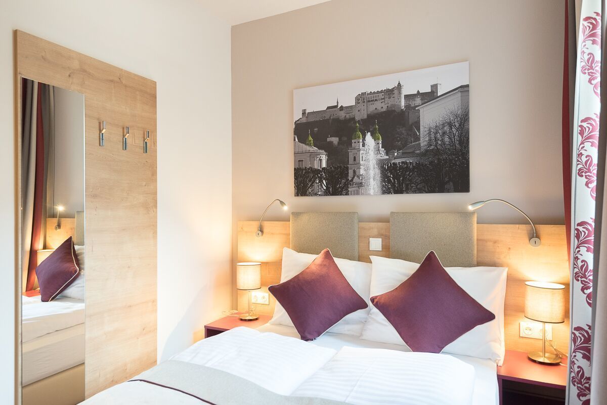 A hotel room with a bed, a large mirror, a picture of a castle, and two bedside lamps.