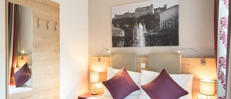 A hotel room with a bed, a large mirror, a picture of a castle, and two bedside lamps.