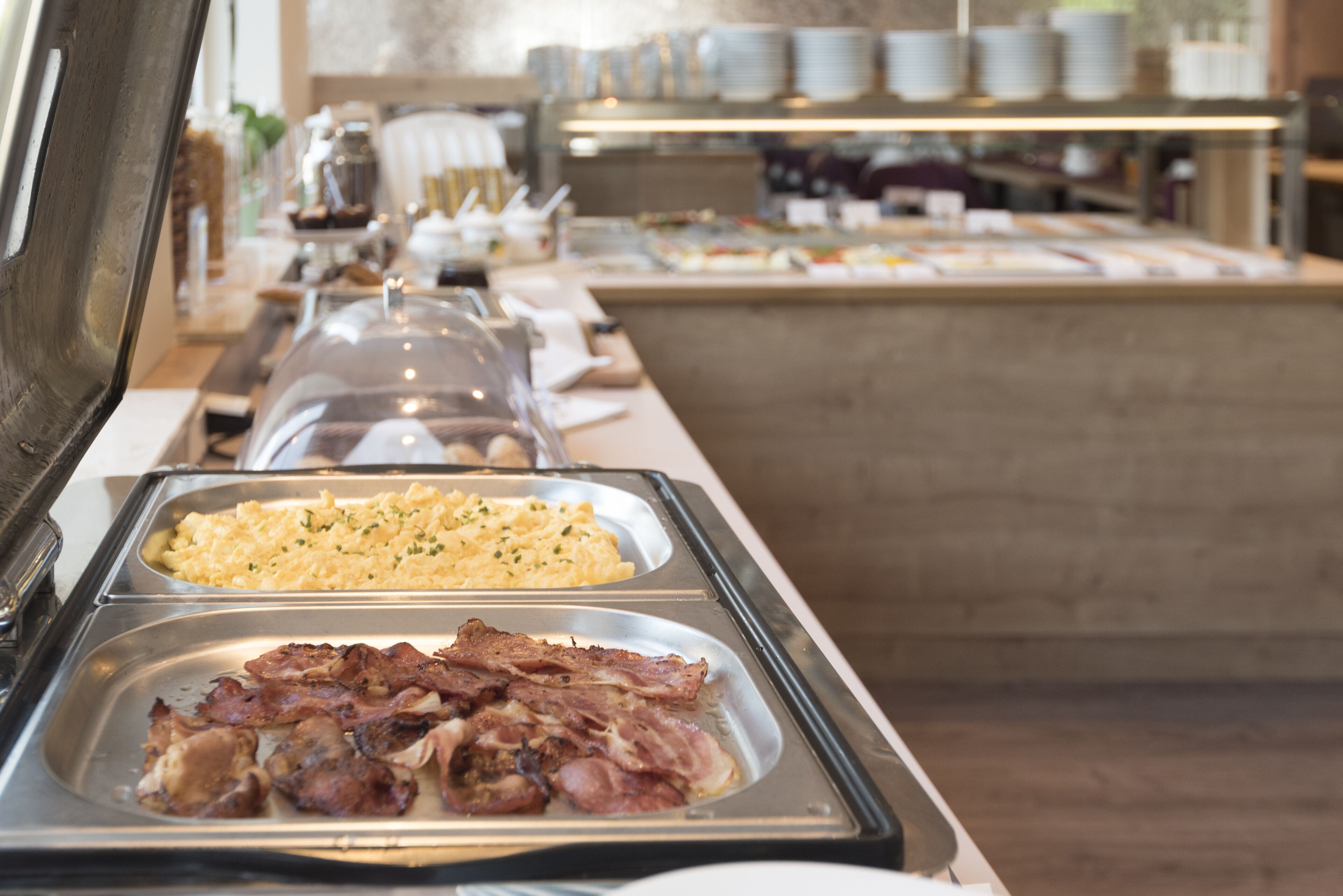 Un bufé con diversas opciones de comida, incluyendo huevos revueltos, tocino y otros platos.