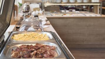 Un buffet proposant une variété de plats, notamment des œufs brouillés, du bacon et d’autres mets.
