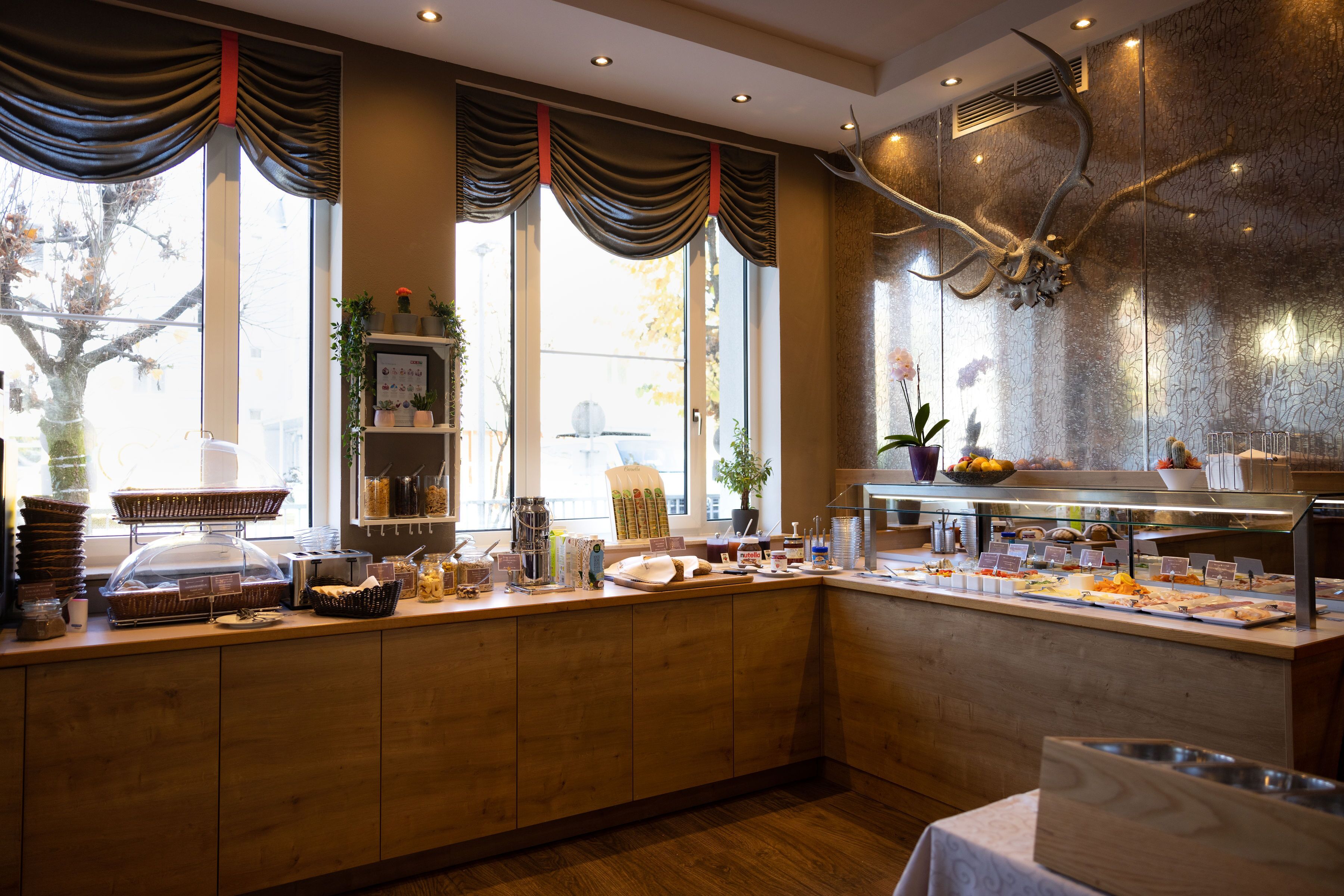 A breakfast buffet area with a wooden counter, various food items, and a decorative antler sculpture.