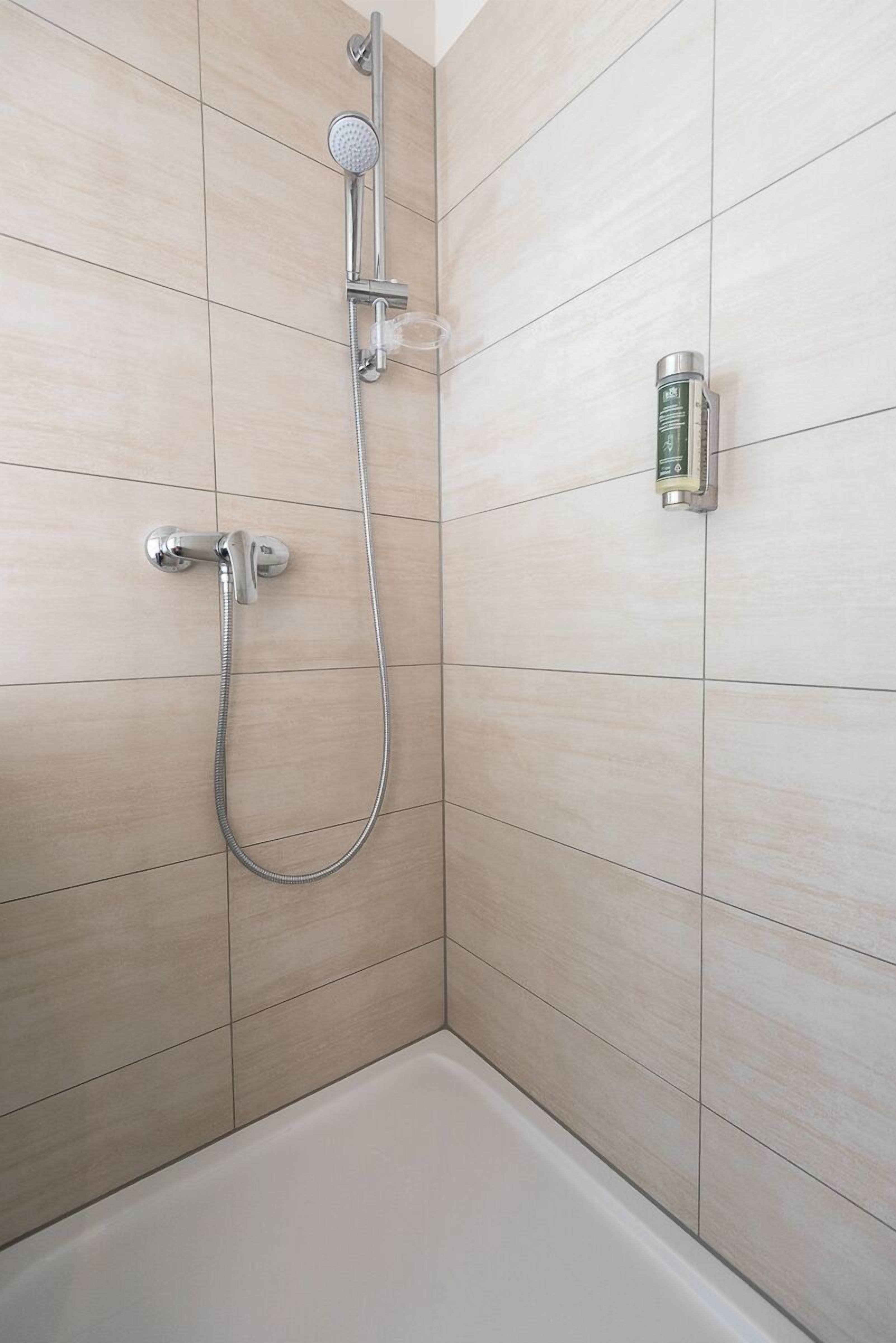 A shower with a handheld showerhead and a wall-mounted faucet.