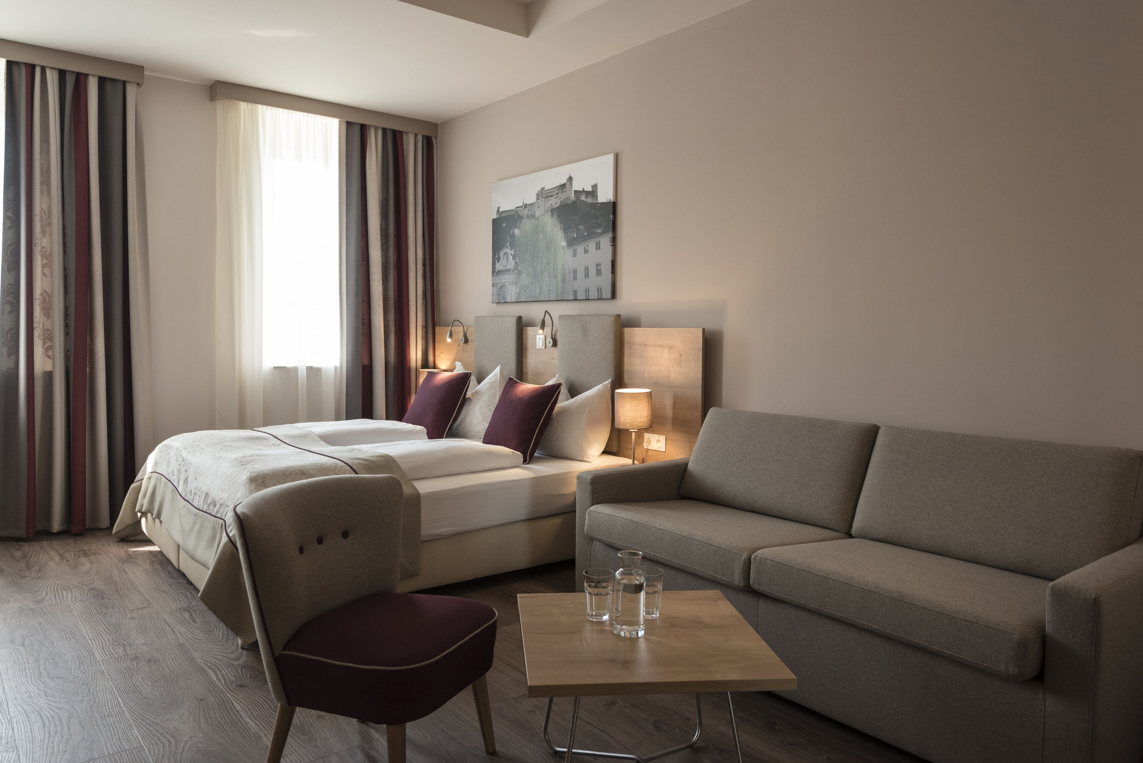 Une chambre d’hôtel avec un lit, un canapé, une chaise, une table basse et un tableau au mur.