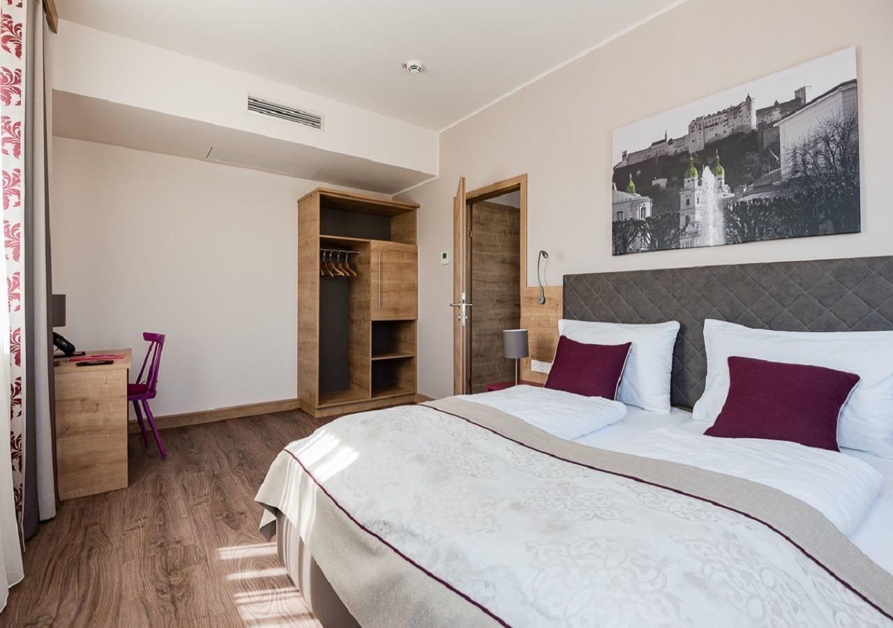 Une chambre à coucher avec un grand lit, une armoire en bois, un bureau avec une chaise et un tableau accroché au mur.