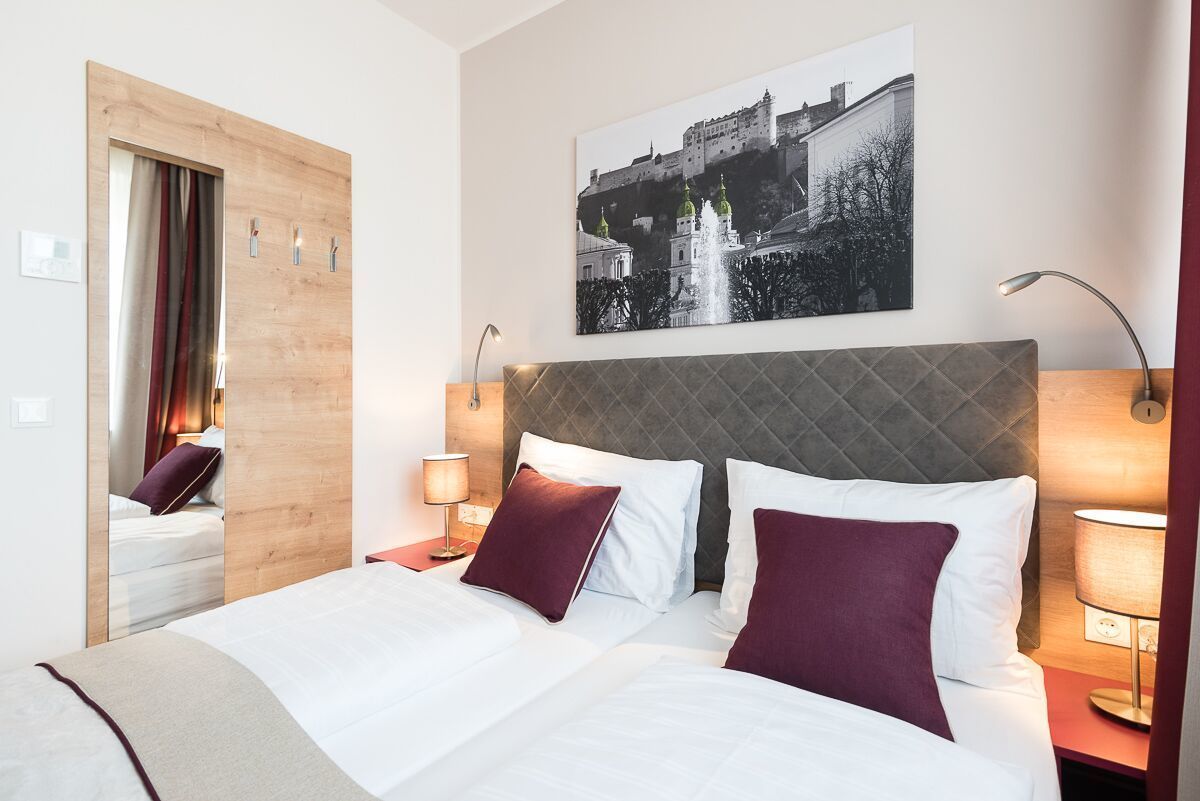 Ein Hotelzimmer mit einem Bett, einem großen Spiegel, einem Wandbild und zwei Nachttischlampen.