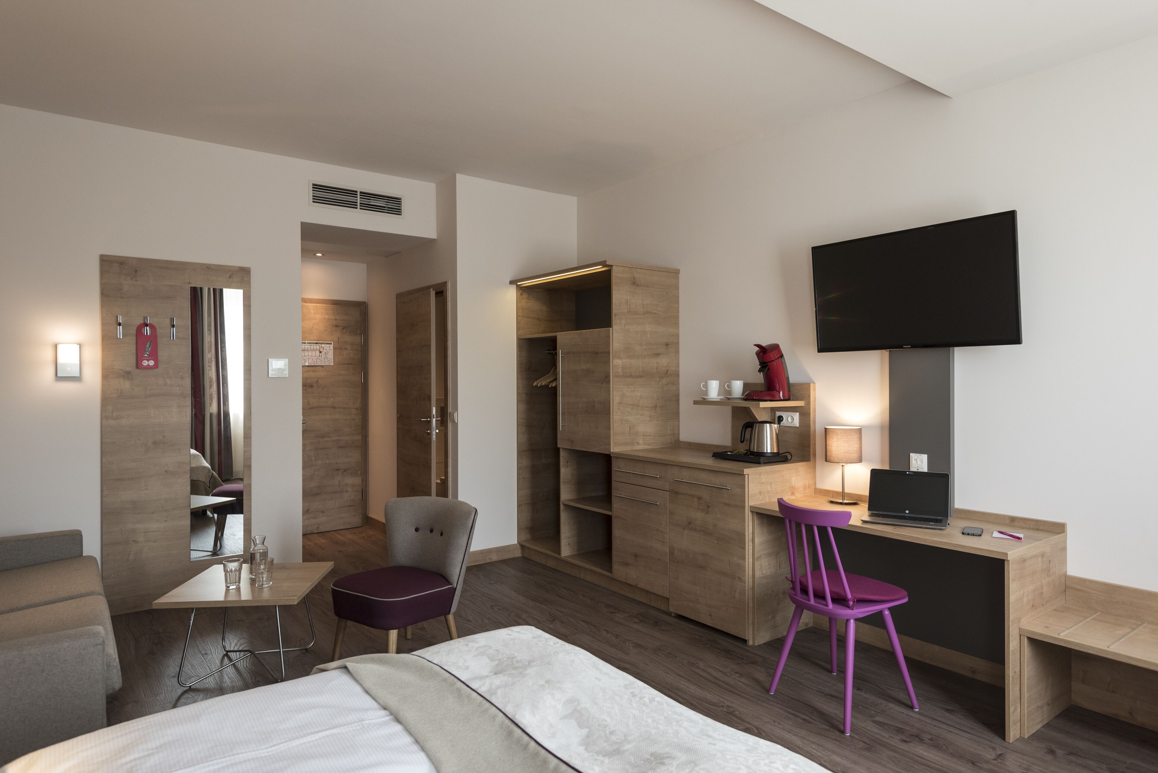 A hotel room with a bed, a desk with a computer, a chair, a TV, and a wardrobe.
