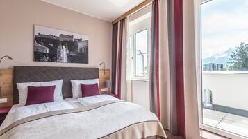 A hotel room with a bed, a headboard, a window with curtains, and a painting on the wall.