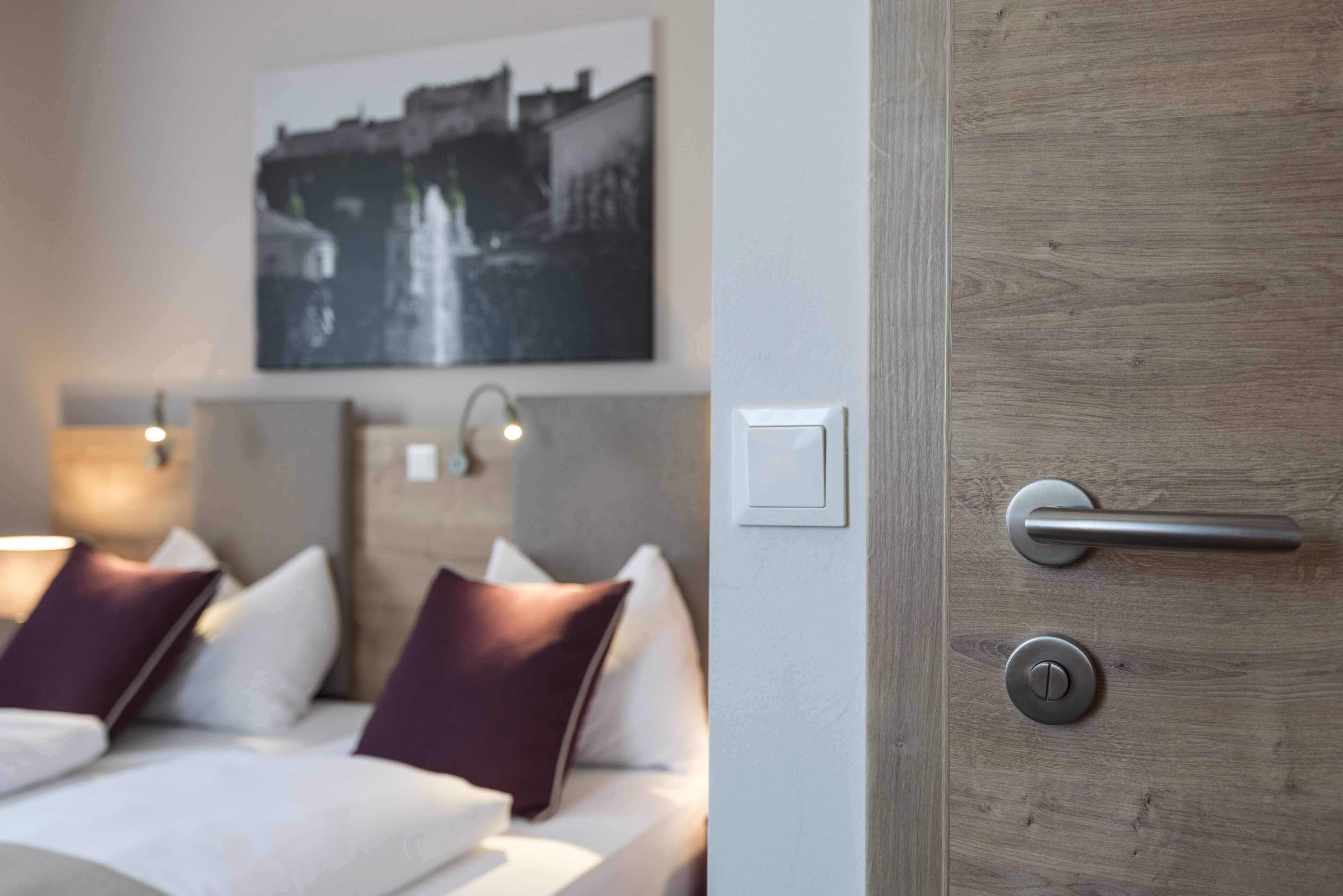 Habitación de hotel con una cama, una lámpara de pared, una puerta con manija e interruptor en la pared.