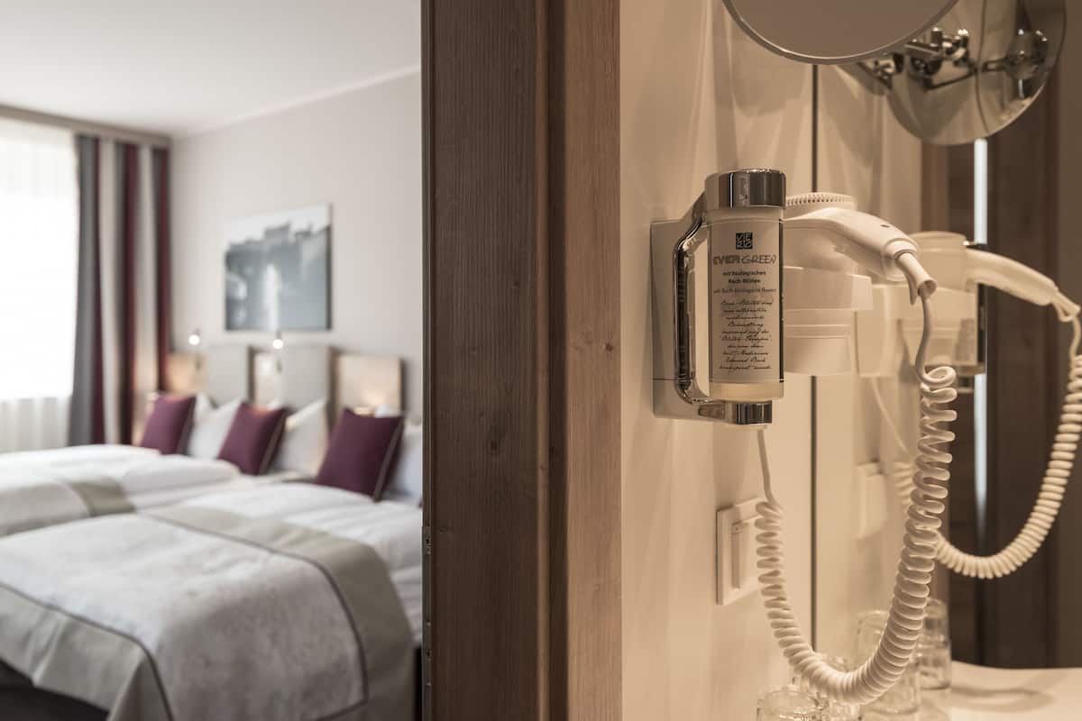 A hotel room with a bed, a mirror, and a hairdryer on the wall.