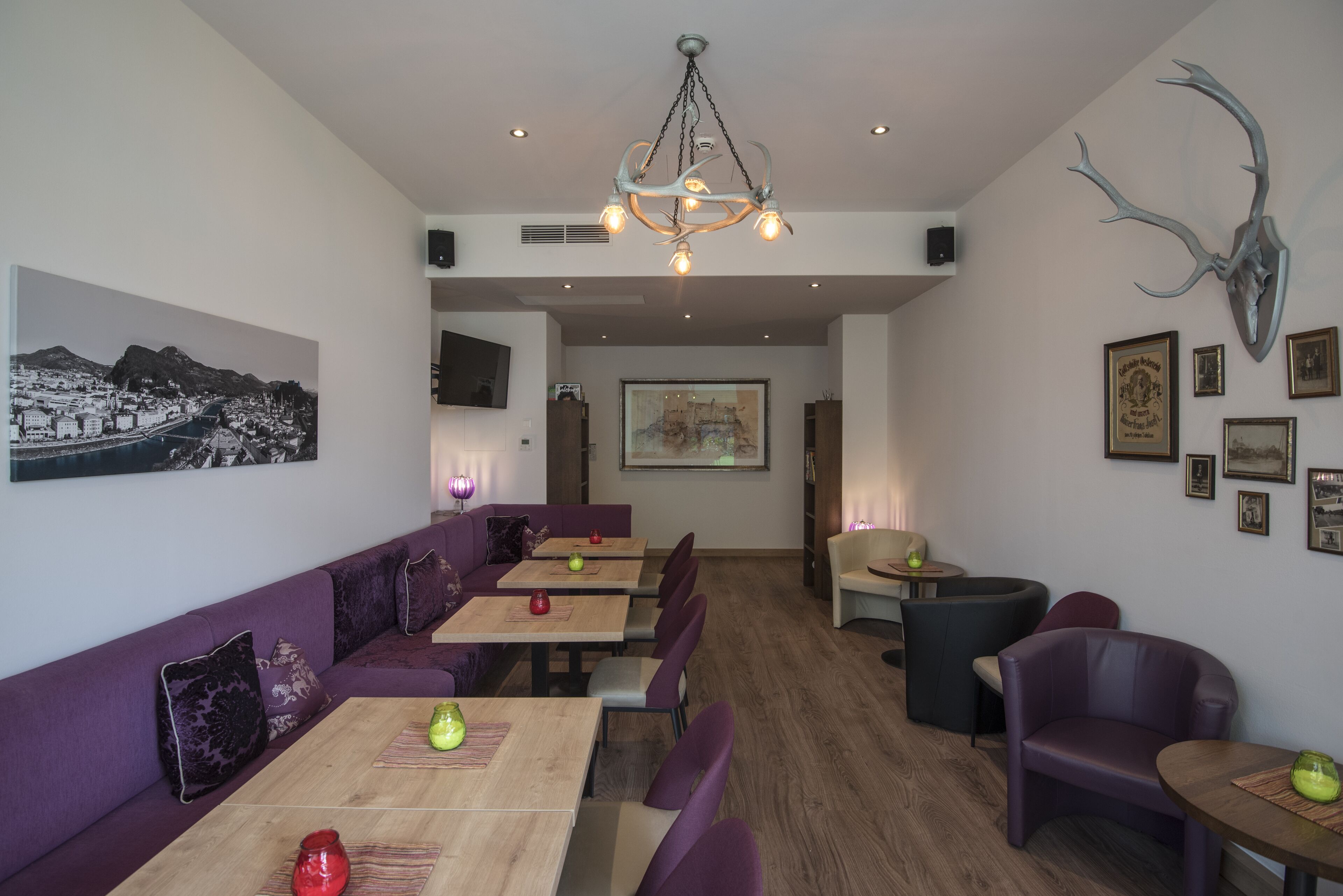 Een restaurant met paarse zittingen, houten tafels en een kroonluchter.