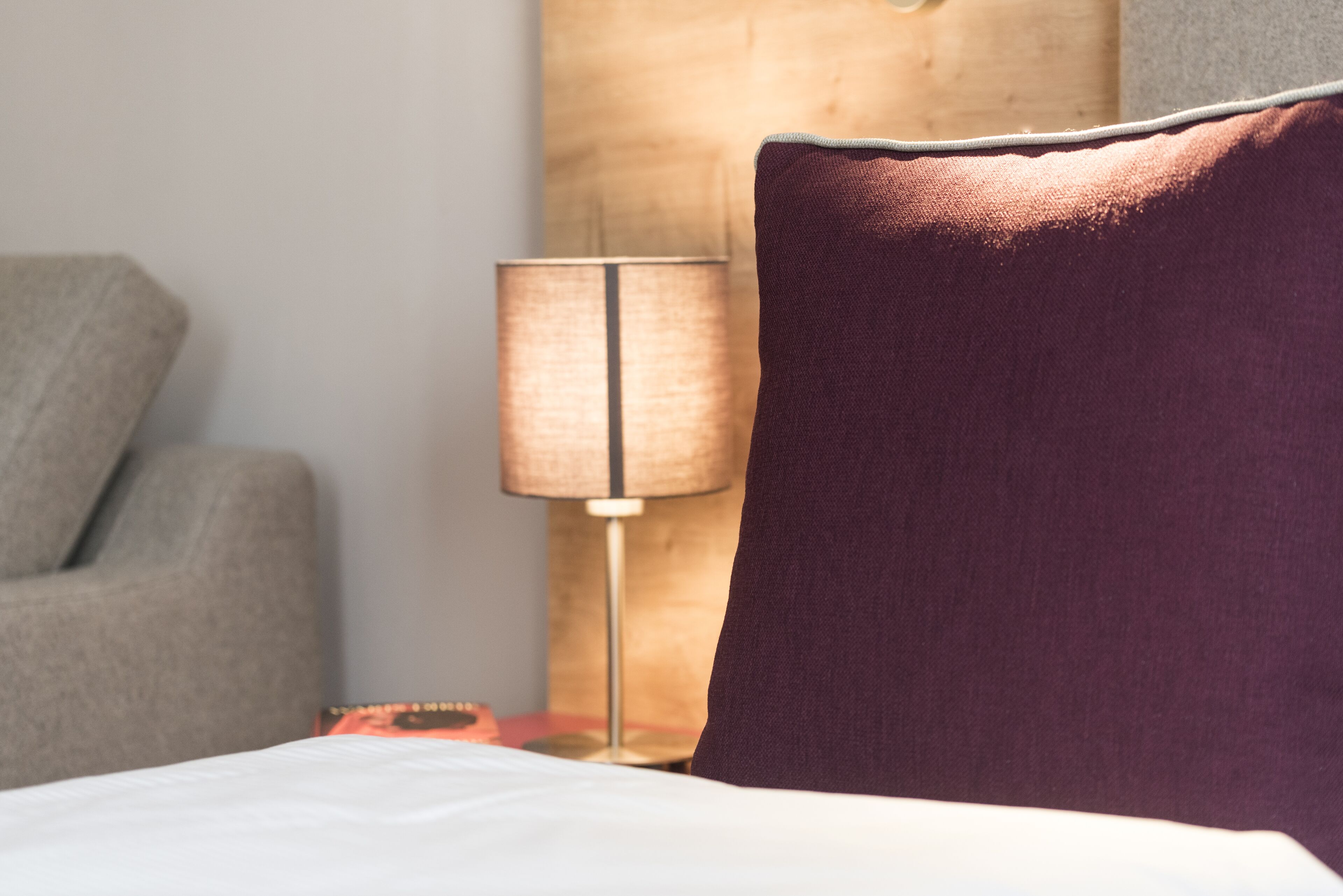 A bed with a white sheet, a purple pillow, a lamp, and a wooden headboard.
