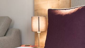 Una cama con sábana blanca, almohada morada, lámpara y cabecero de madera.