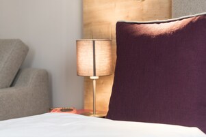 Un lit avec un drap blanc, un oreiller violet, une lampe et une tête de lit en bois.