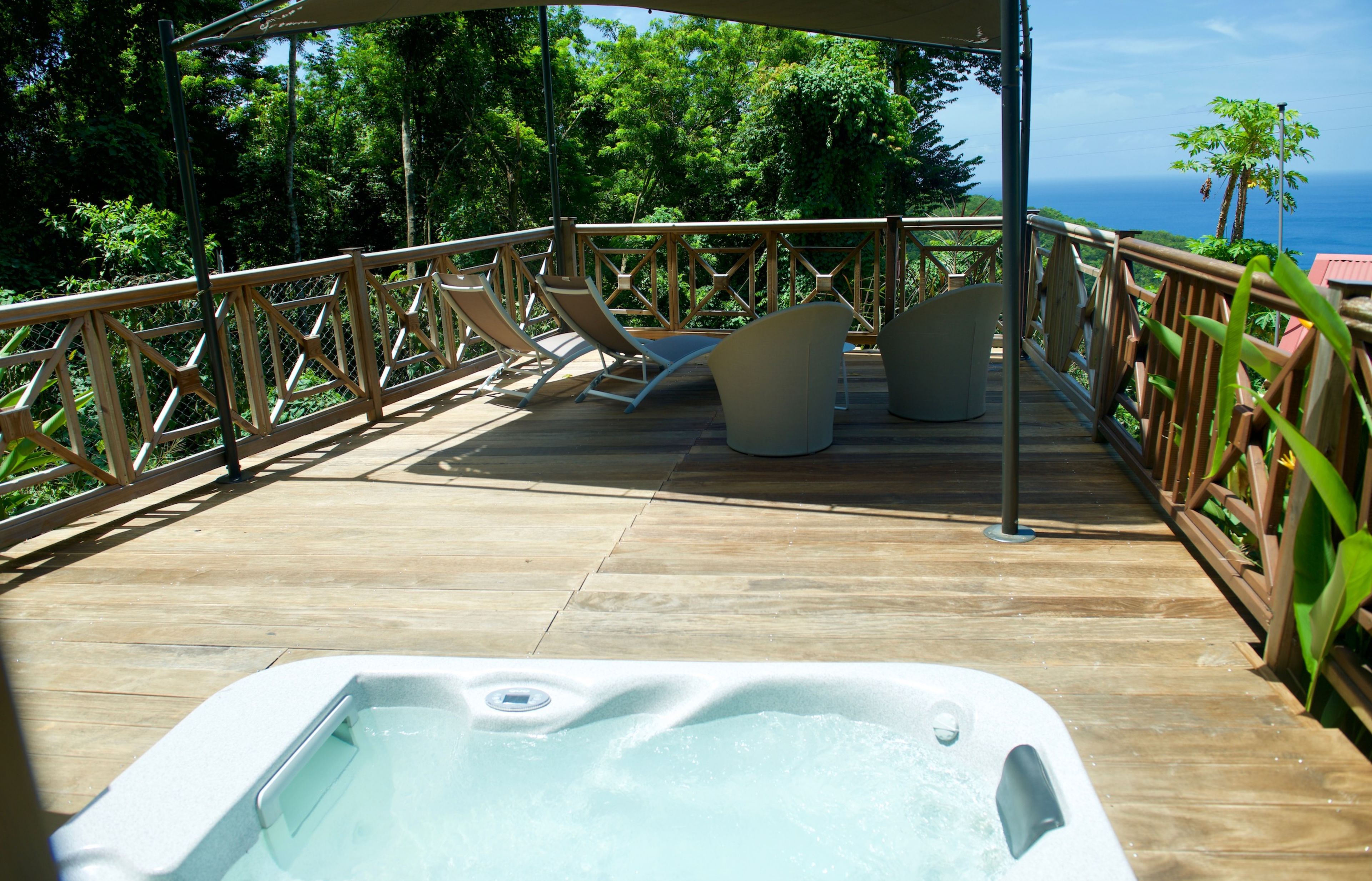 Una terraza de madera con un jacuzzi, sillas de descanso y vista al océano.