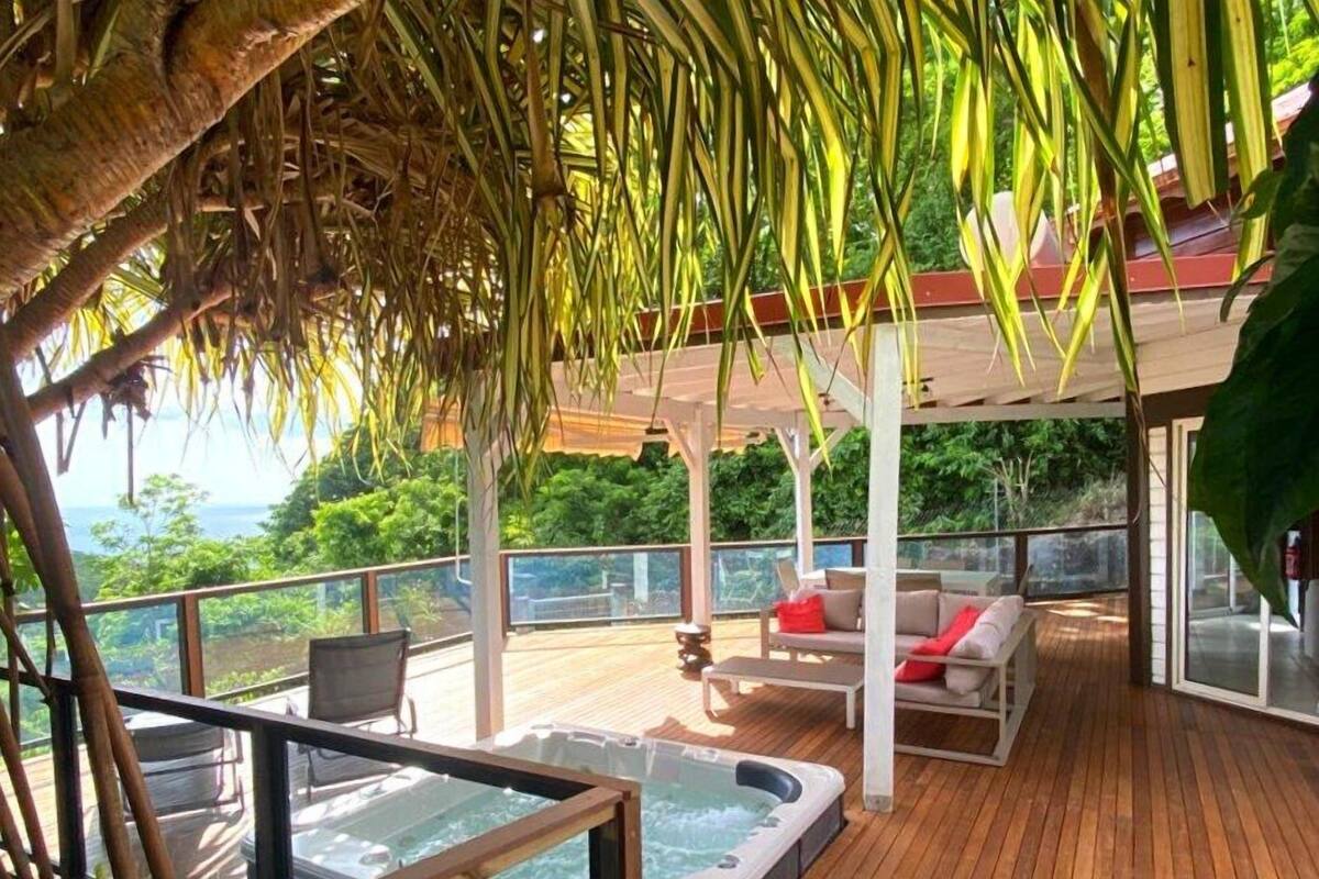 Una terraza de madera con jacuzzi, asientos exteriores y vista al océano.