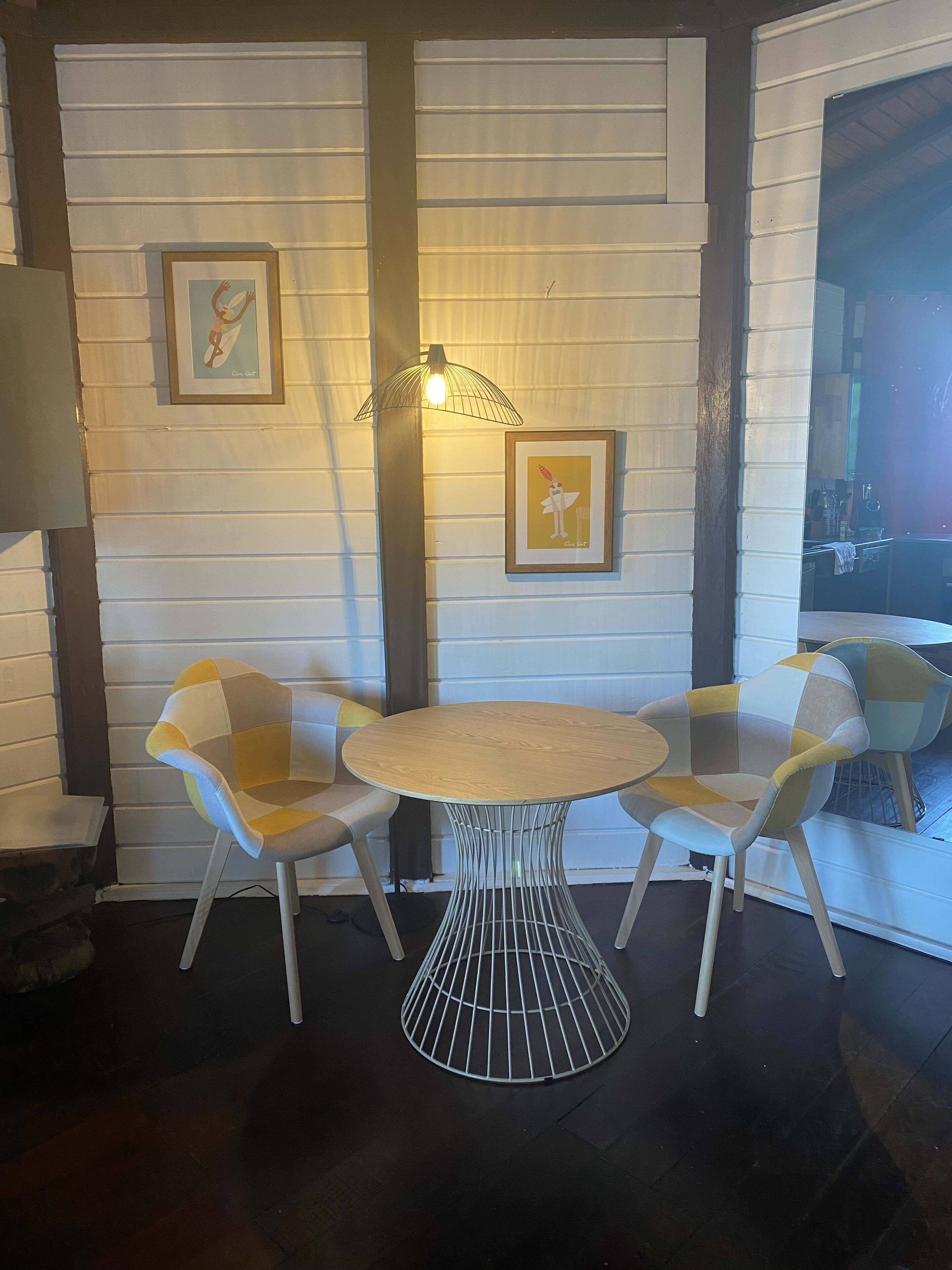 A dining area with a round table and four chairs, framed artwork on the wall, and a hanging light fixture.