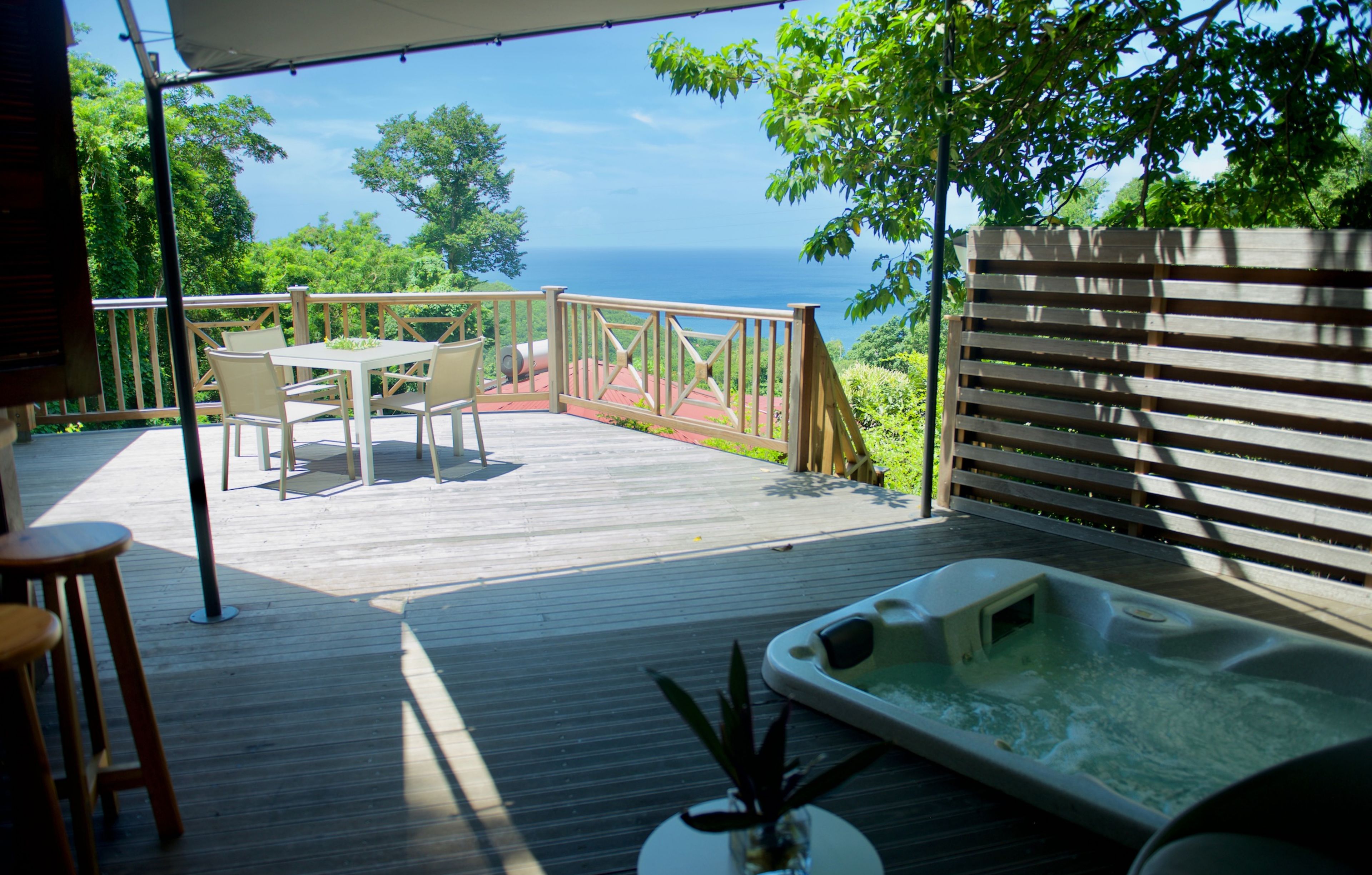 Une terrasse en bois avec un jacuzzi, une table et des chaises, et une vue sur l’océan.