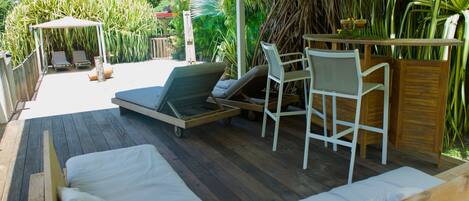 Un espacio de estar al aire libre cubierto, con mobiliario de madera, incluyendo un sofá y sillas, bajo una marquesina.