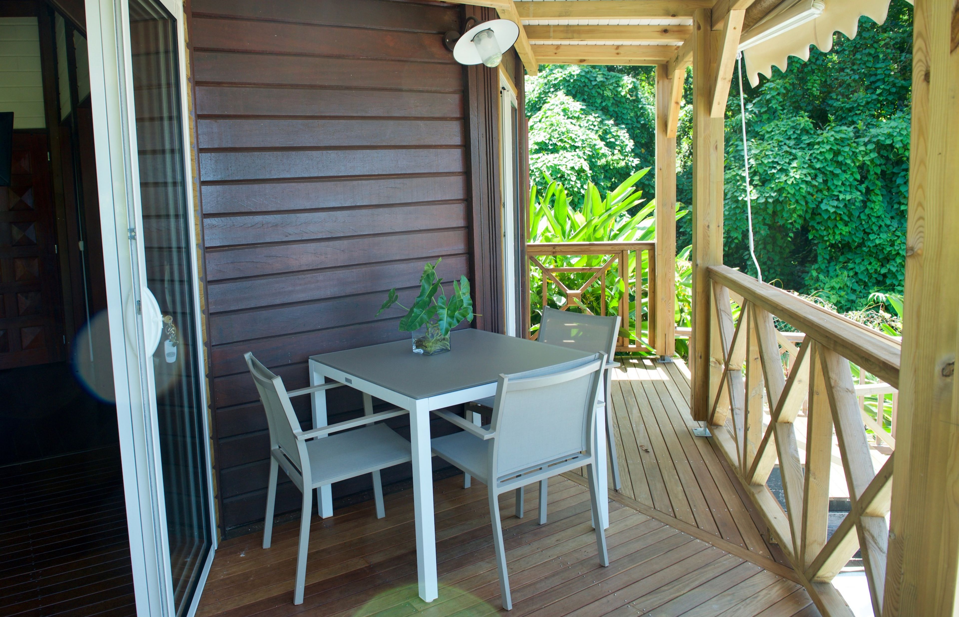 A wooden deck with a table and chairs, surrounded by a railing and greenery.