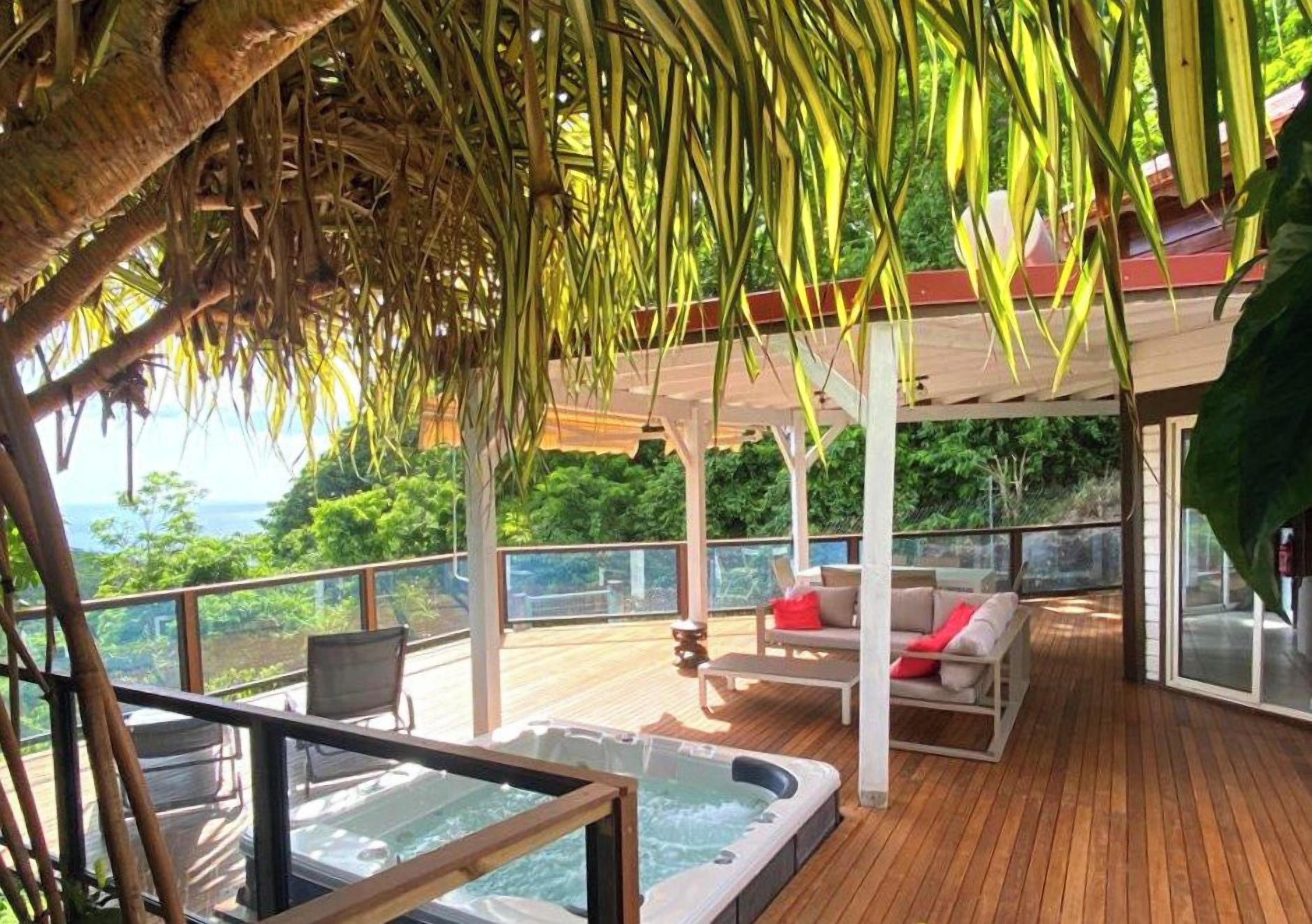 A wooden deck with a hot tub, outdoor seating, and a view of the ocean.