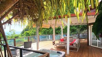 A wooden deck with a hot tub, outdoor seating, and a view of the ocean.
