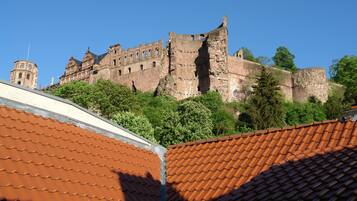 Un castillo histórico con una torre destacada y murallas almenadas, rodeado de exuberante vegetación.