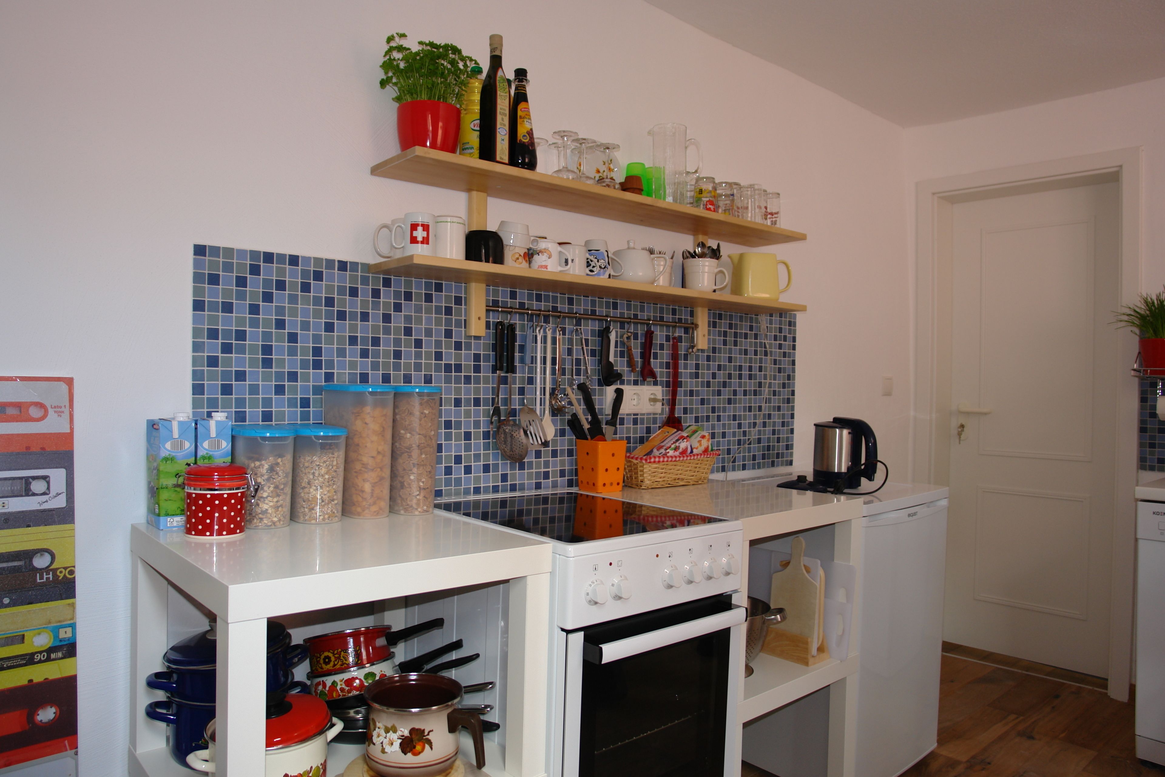 A compact kitchen with a white stove, oven, and countertop. There are shelves above holding various kitchen items and a potted plant.