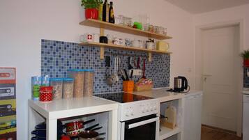 A compact kitchen with a white stove, oven, and countertop. There are shelves above holding various kitchen items and a potted plant.