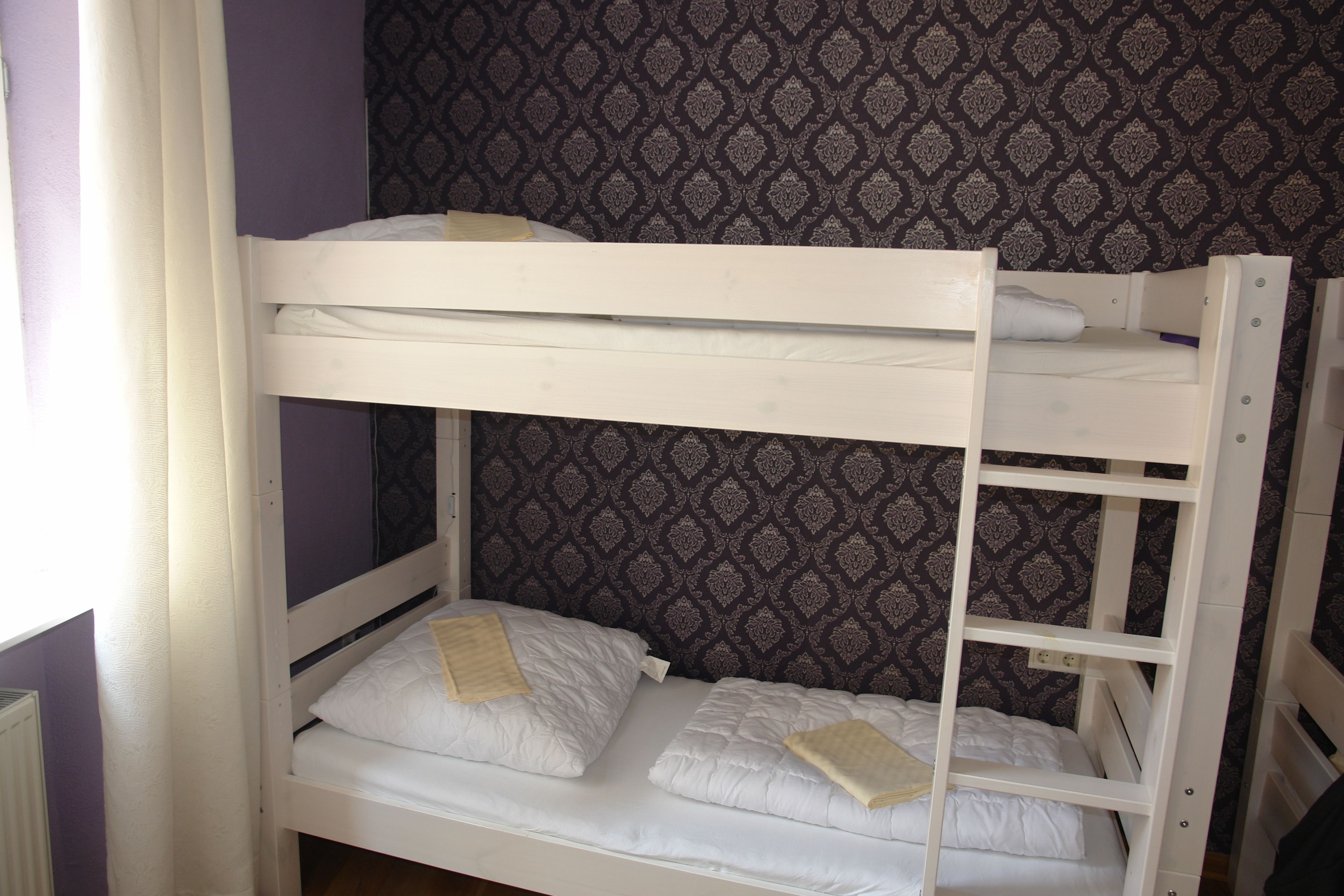 A bunk bed with two levels, white bedding, and a patterned wallpaper background.