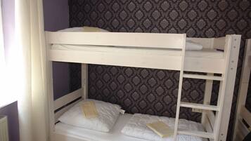 A bunk bed with two levels, white bedding, and a patterned wallpaper background.