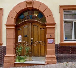 A wooden double door with a glass panel, a brick wall, and a window to the right. - Lotte Hostel (Heidelberg)