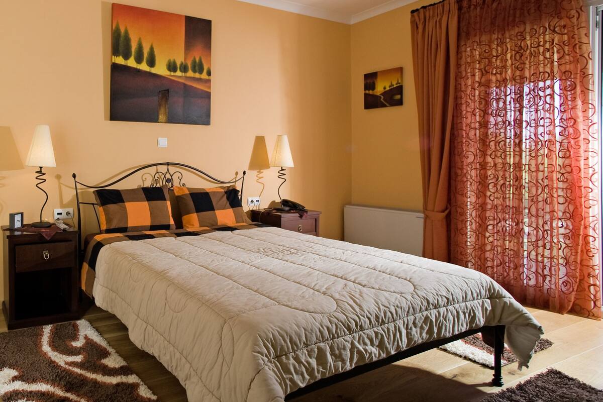A bedroom with a bed, nightstands, a chair, a desk, and a window with curtains.