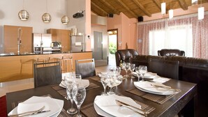 Una cocina moderna con armarios de madera, electrodomésticos de acero inoxidable y una zona de comedor preparada para una comida, con una mesa dispuesta para seis personas.