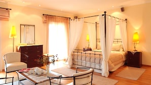 Un dormitorio con cama con dosel, lámparas de noche, cómoda, una silla y una mesita con un florero.